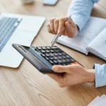 Person working on bookkeeping in Canada with a laptop, calculator, and pen on a desk